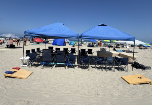 Large beach setup event with canopy with lounge chairs, towels, cooler, and beach setup at Mission Beach in San Diego.